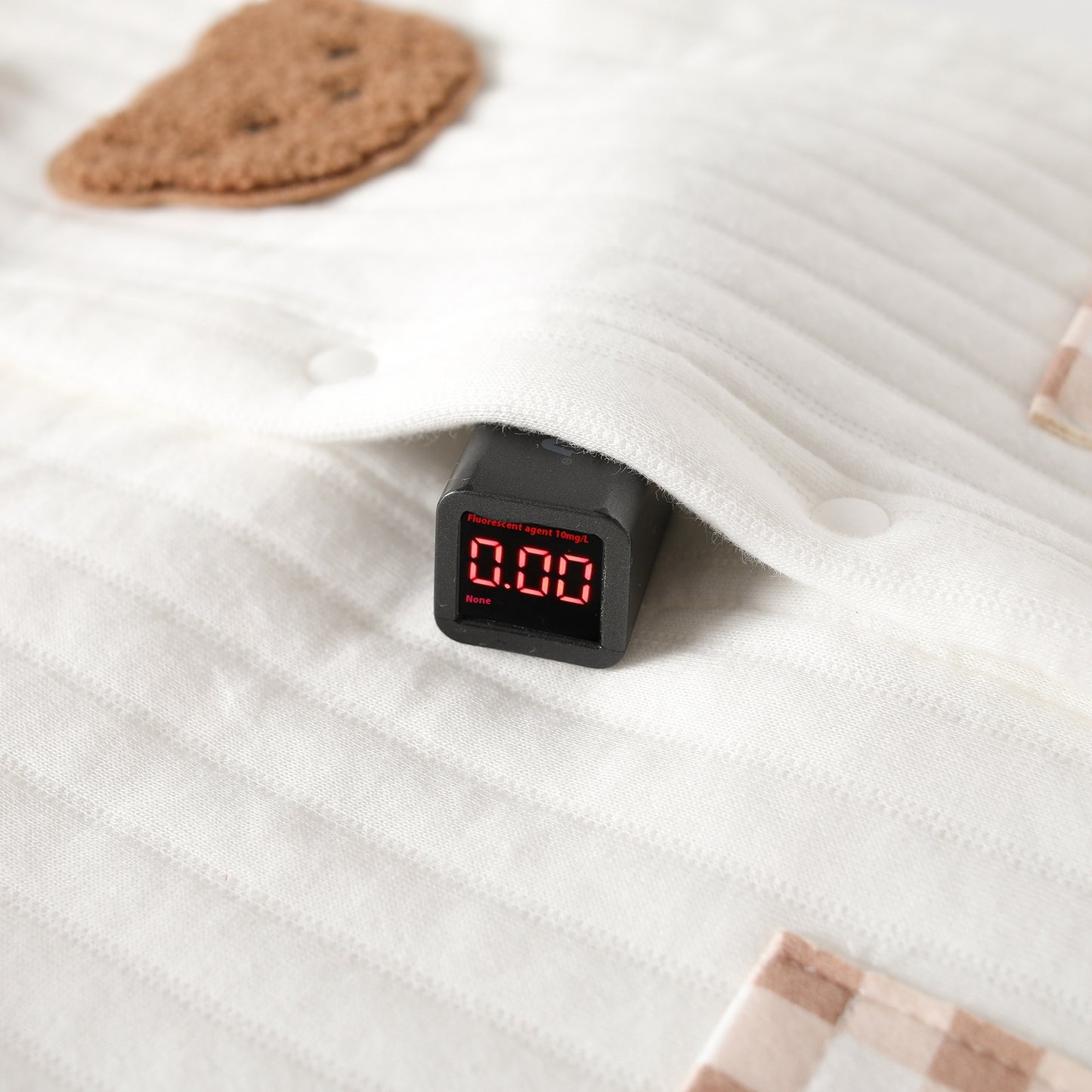 生地の蛍光テストを示すデジタル測定器とコットン素材のクローズアップ