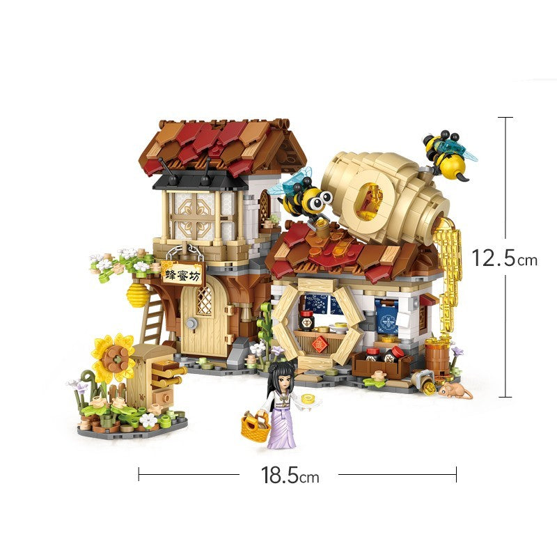 蜂蜜工房をテーマにしたミニブロックセット。木造フレームの二階建て家屋、赤茶色の瓦屋根、大きな蜂蜜樽と滴るハニーパーツ、巣箱や花畑など細部まで精巧に再現。小物付きの庭エリア、ひまわり装飾、蜂のフィギュア、和装の人物ミニフィグが付属。幅約18.5cm・高さ約12.5cmで存在感あるディスプレイモデル。創造力と集中力を育てる知育ブロック玩具。