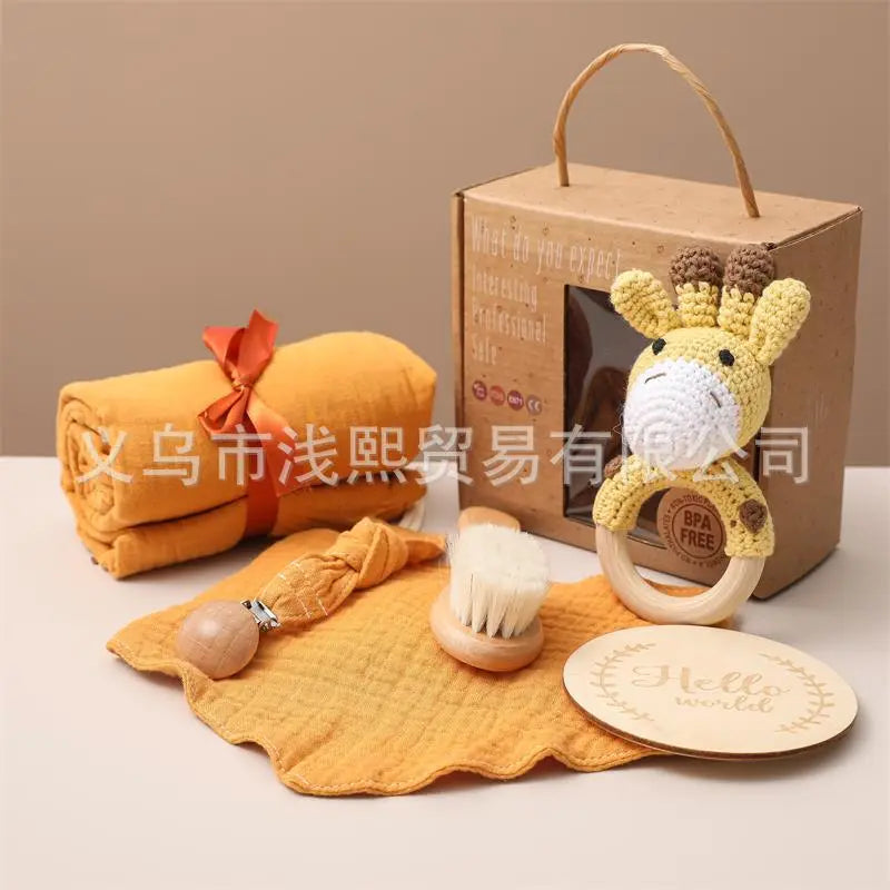マスタードイエローのタオルロールとキリンモチーフのラトル、スタイ、木製ブラシ、HELLO WORLDプレートをクラフトボックスと一緒に並べたベビーギフトセットの写真