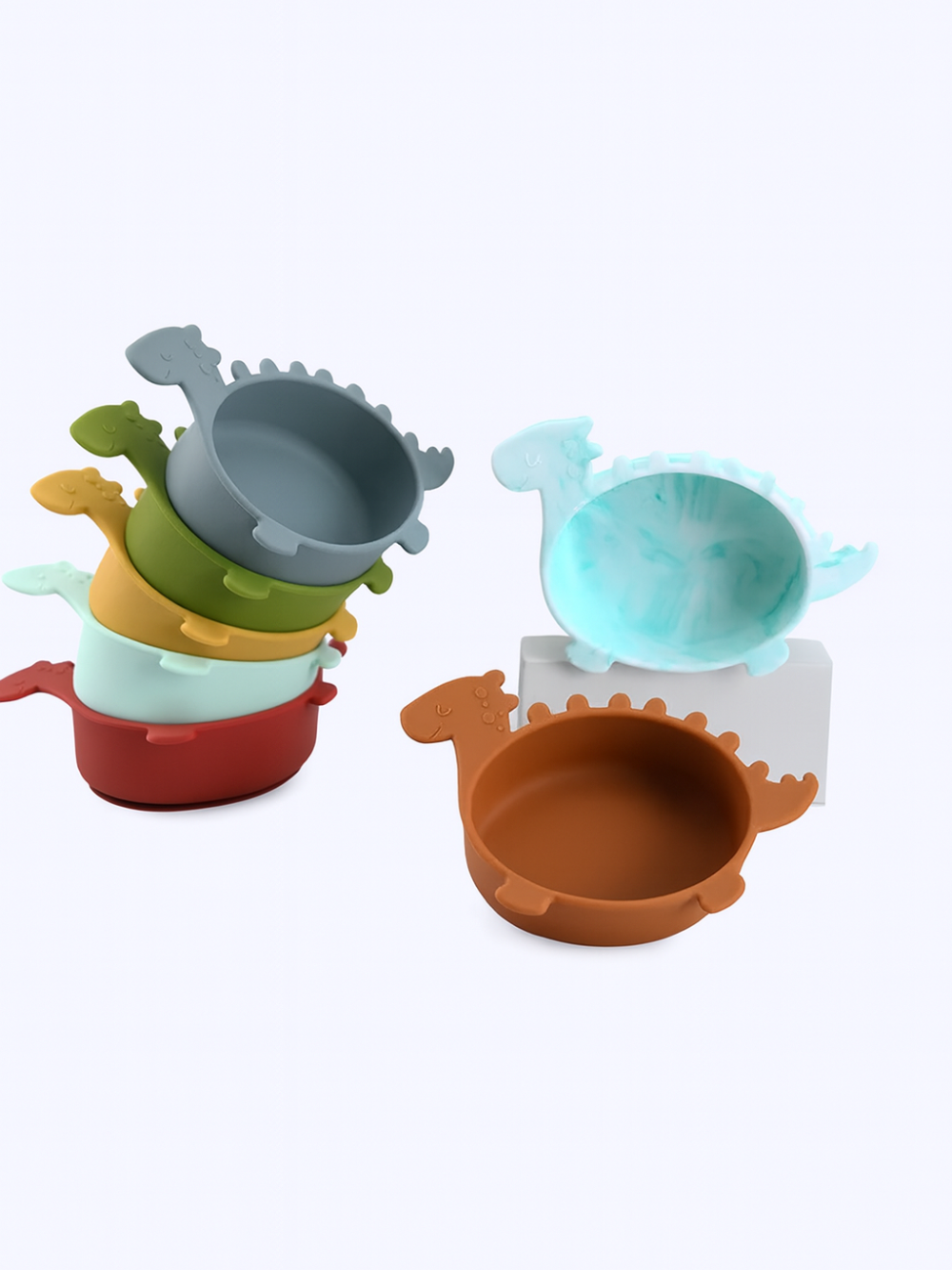 白いスタジオ背景の上に、くすみカラーの恐竜型シリコンベビーボウルが積み重ねて並んでいる様子の商品写真
