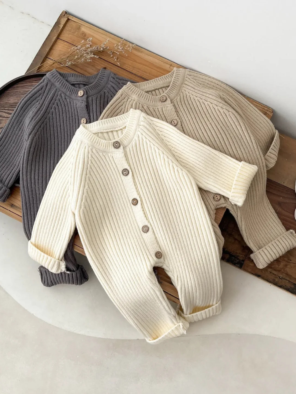 リブ編みデザインの長袖ニットベビーロンパースが色違いで重なって並んだイメージ
