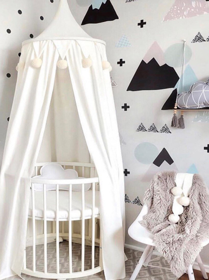 山柄のウォールデコを背景に、白いドーム型キャノピーが丸型ベビーベッドをふんわり包み込むナチュラルな子ども部屋インテリア（ホワイト天蓋・ベビーベッドキャノピー）
