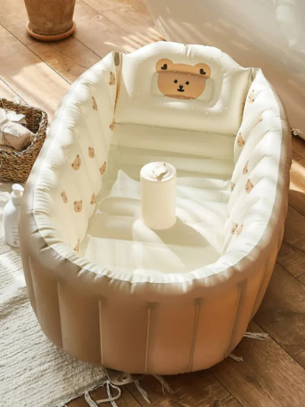 木目フロアとラグの上に、くまの顔付きヘッドレストが付いたベージュの空気式ベビーバスを置いた室内シーン（くま柄インフレータブルベビーバス）
