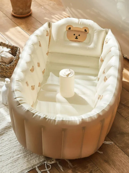 木目フロアとラグの上に、くまの顔付きヘッドレストが付いたベージュの空気式ベビーバスを置いた室内シーン（くま柄インフレータブルベビーバス）
