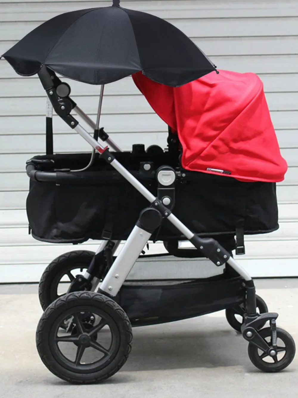 赤いシートのベビーカーに黒い日よけ傘を取り付けて屋外を走行している様子(ベビーカー 日よけ 傘 ブラック)

