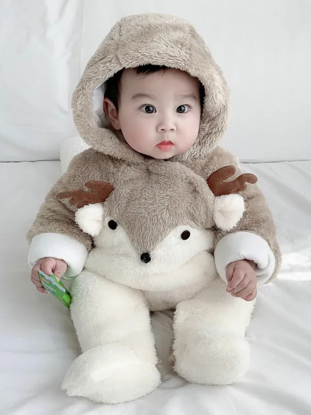 耳付きフード付きカーキ子鹿デザインのもこもこベビーカバーオールを着て正面を向いて座る赤ちゃん
