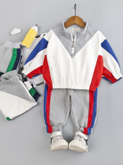 レッドとブルー配色トップスとグレー長ズボンにスニーカーを合わせた男の子用スポーツセットアップコーデ
