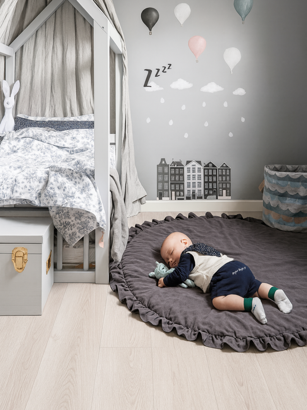 子ども部屋の床に敷いたダークグレーの円形フリル付きベビープレイマットの上で寝転ぶ赤ちゃん 室内の使用イメージ
