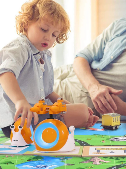 子どもがプレイマットの上で、上部にプロペラが付いたオレンジと白のカタツムリ型おもちゃで遊んでいる様子（後ろに大人が見える）。
