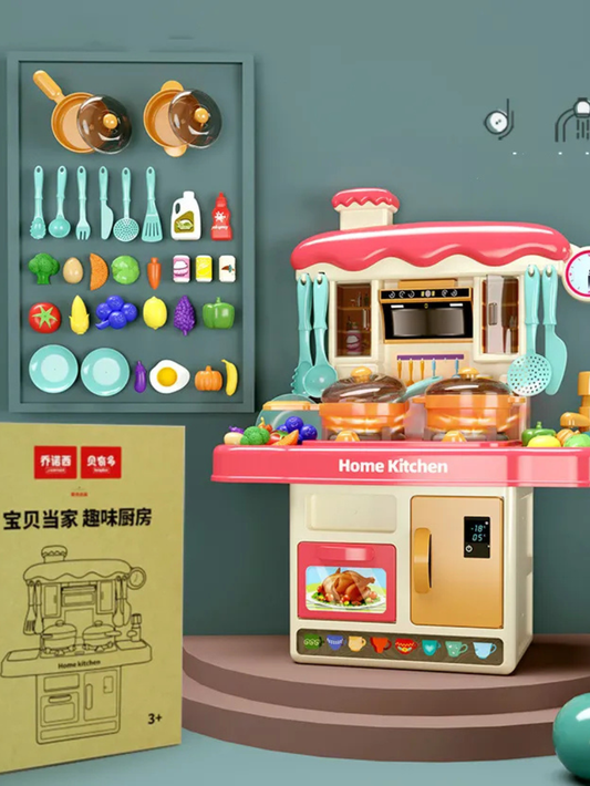 スタジオのグリーン背景で撮影された子ども用おままごとキッチンセット。ピンクの屋根とターコイズのアクセント付きキッチン本体、横に調理器具が並ぶアクセサリーボードと商品箱が置かれている。
