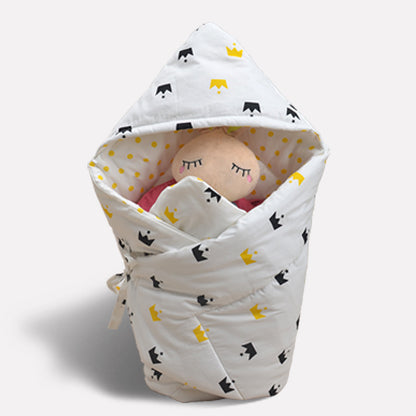 ホワイト地にイエローとブラックの王冠柄が入ったベビーおくるみにぬいぐるみの赤ちゃんがくるまれている写真（ベビーおくるみ 王冠柄 ホワイト）
