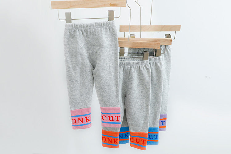 裾にカラフルな切り替えが入ったグレータイツパンツをハンガーに掛けた子ども用ボトムス
