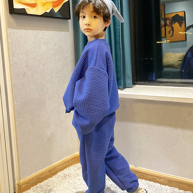 ブルー無地セットアップを着た男の子が横向きで立ち、ポケットに手を入れたままカメラを見つめている全身コーデイメージ
