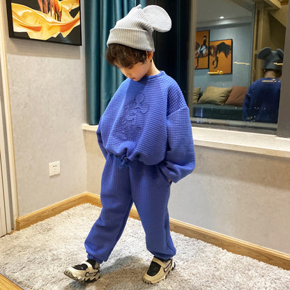 室内でブルー無地セットアップを着た男の子がまっすぐ立っている全身コーディネートイメージ
