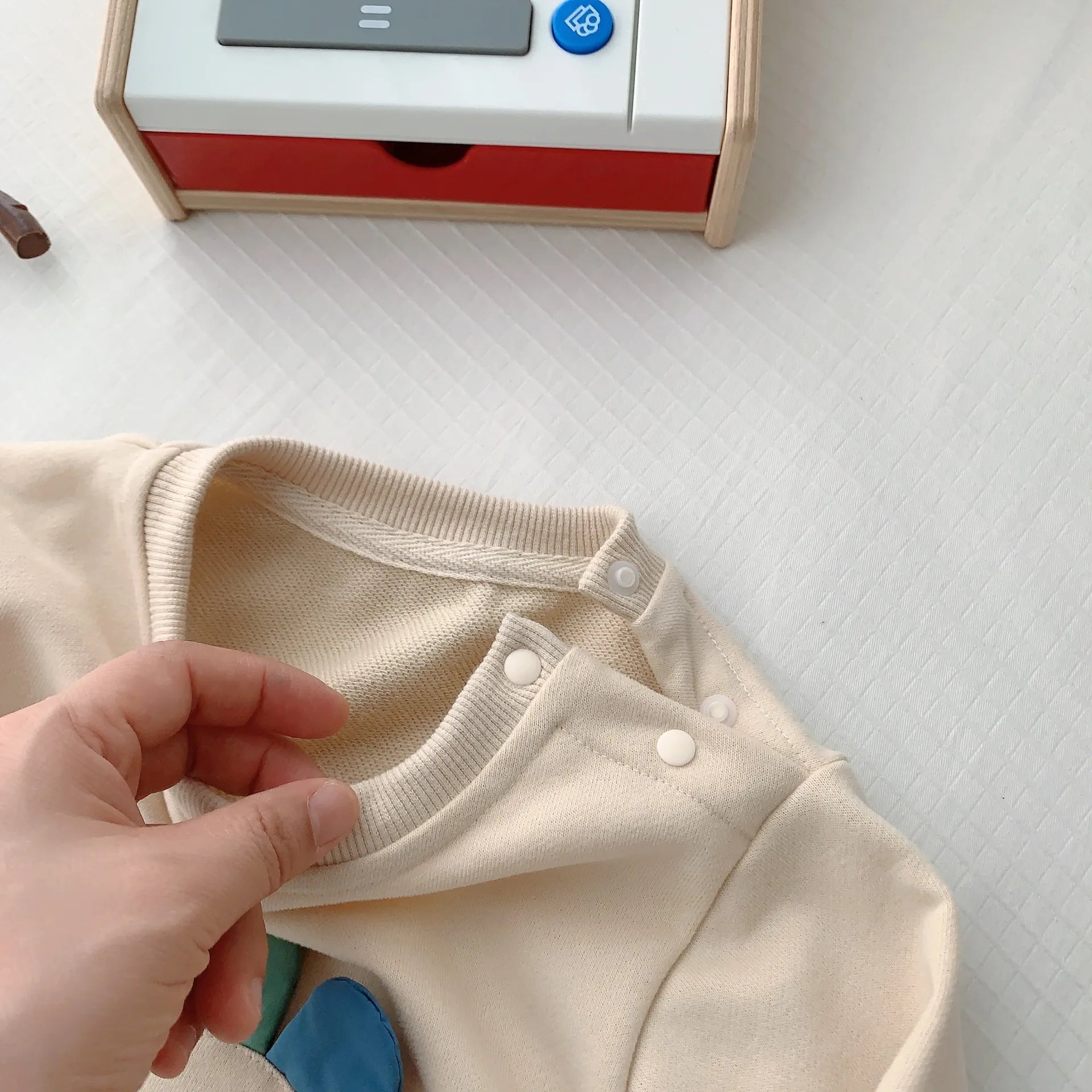 片側スナップボタン付きラウンドネックの首まわりディテールが分かるベビーロンパースのアップ
