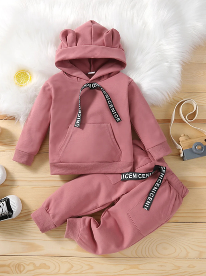 ピンクのフード付き長袖トップスとロングパンツのニットセットアップを木目の床に平置きしたコーデ一式
