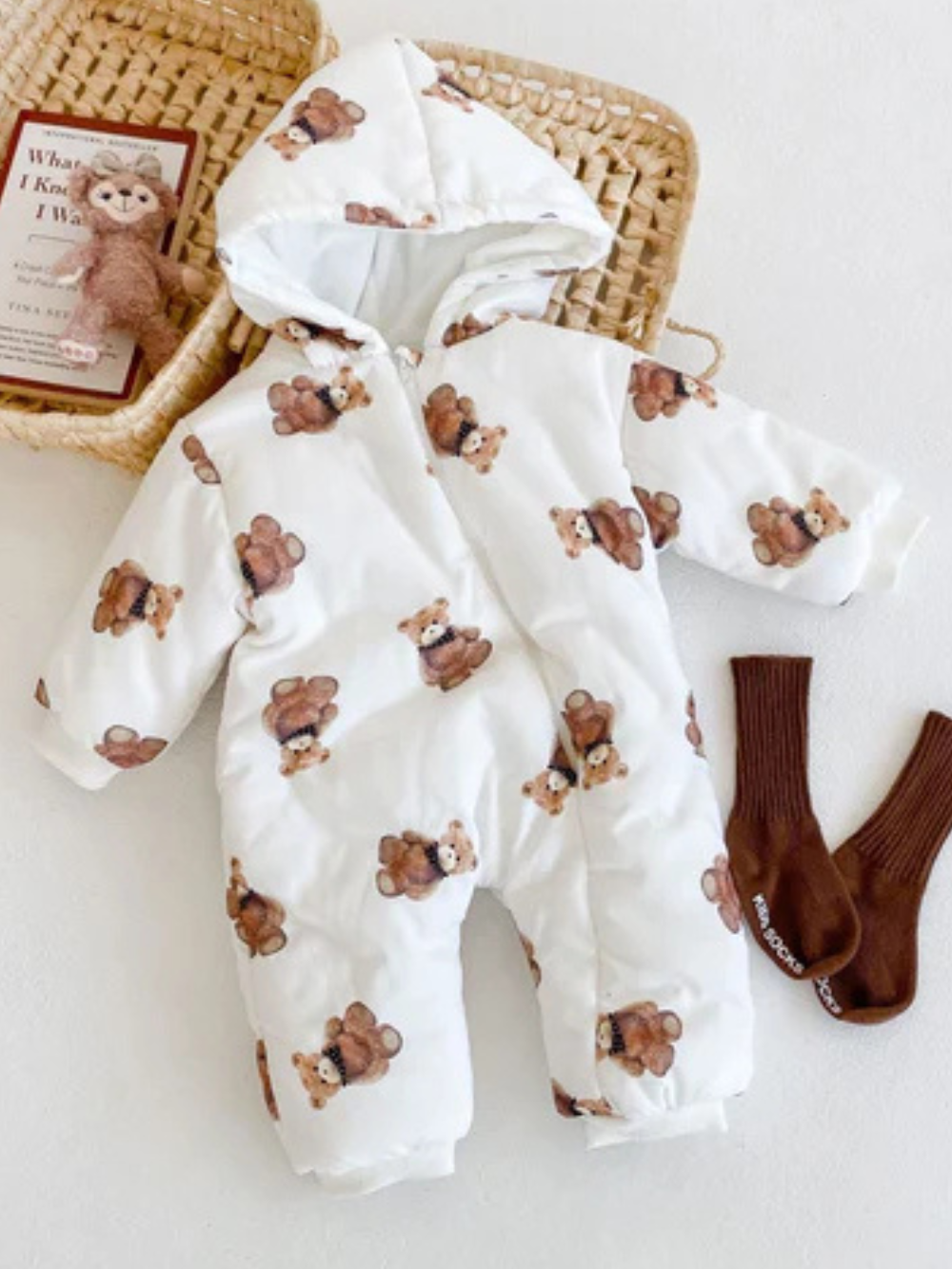 くま柄フード付きベビーカバーオールとバスケット、丸めたベビーソックスを並べた冬コーデのフラットレイ画像
