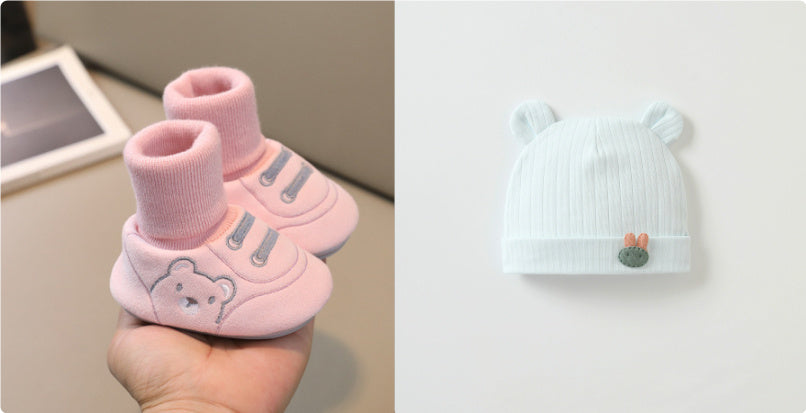 大人の手のひらに載せた11〜13cm赤ちゃん用 室内向けやわらか布ルームシューズ 滑り止め付き 靴下一体型 ピンク と となりに置かれたくま耳付きベビーニット帽のやさしいカラーが分かる室内撮影写真

