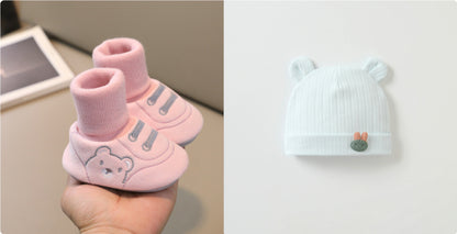 大人の手のひらに載せた11〜13cm赤ちゃん用 室内向けやわらか布ルームシューズ 滑り止め付き 靴下一体型 ピンク と となりに置かれたくま耳付きベビーニット帽のやさしいカラーが分かる室内撮影写真
