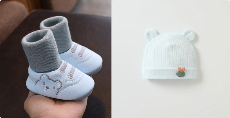 大人の手のひらに載せた11〜13cm赤ちゃん用 室内向けやわらか布ルームシューズ 滑り止め付き 靴下一体型 ブルー×グレー と となりに置かれたくま耳付きベビーニット帽のやさしいカラーが分かる室内撮影写真
