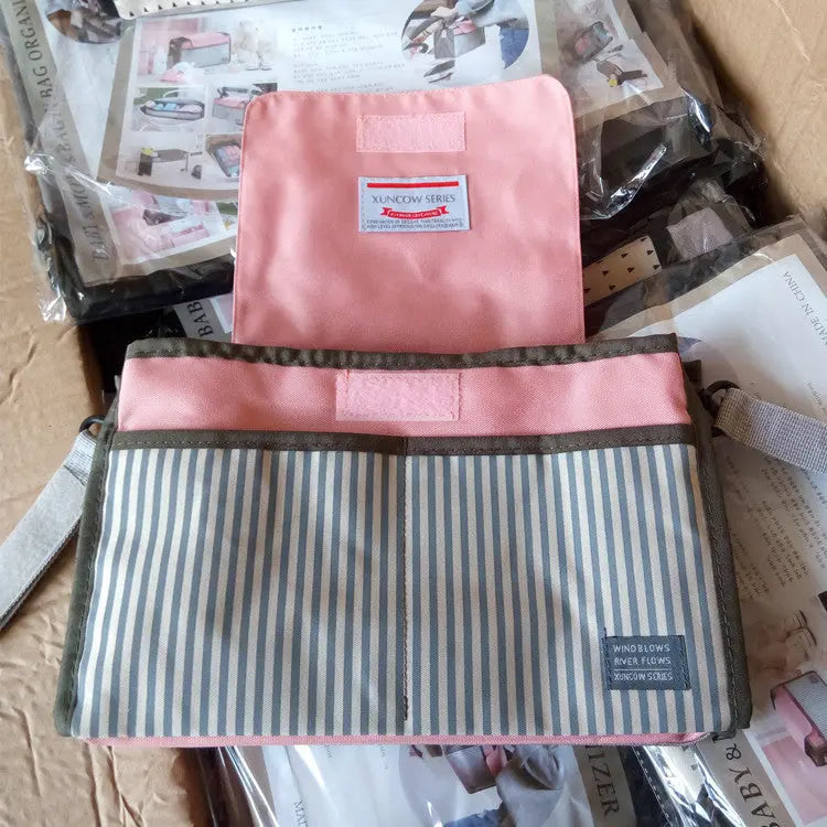 ピンクのフラップ付きマザーズバッグとベビーグッズが並ぶ写真（ママバッグ）
