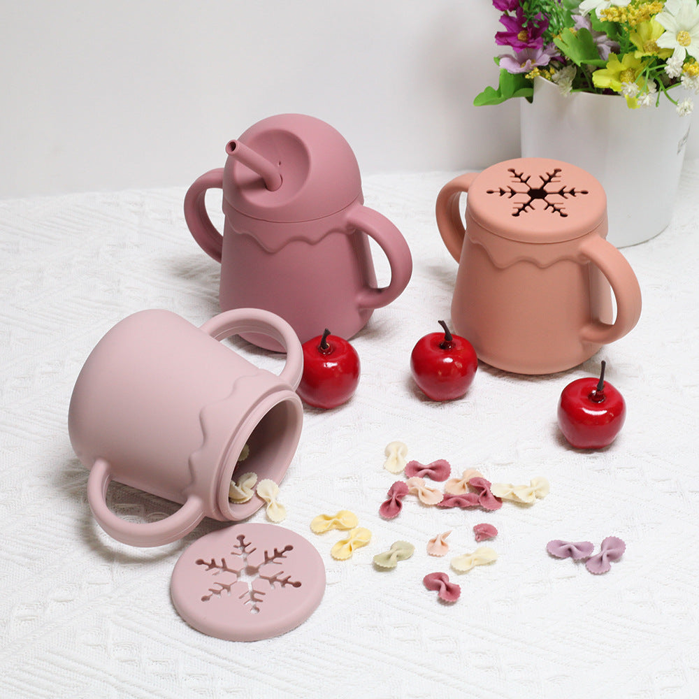 ピンクのシリコン2in1ベビーカップと外したフタ、周りにこぼれたスナックが写っている画像（ノースピルベビーカップ）
