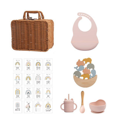 ラタン風バスケットとピンクのシリコンビブ、レインボーカード、アニマルスタッキングおもちゃ入りボウル、ピンクのシリコンカップとスプーン＆ボウルが並んだセット画像（ベビー用シリコン知育＆テーブルウェアスーツ）
