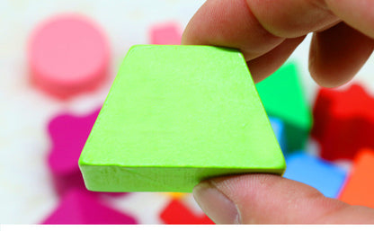 指でつまんだ黄緑色の木製ブロックと背景にぼかして映るカラフルな積み木