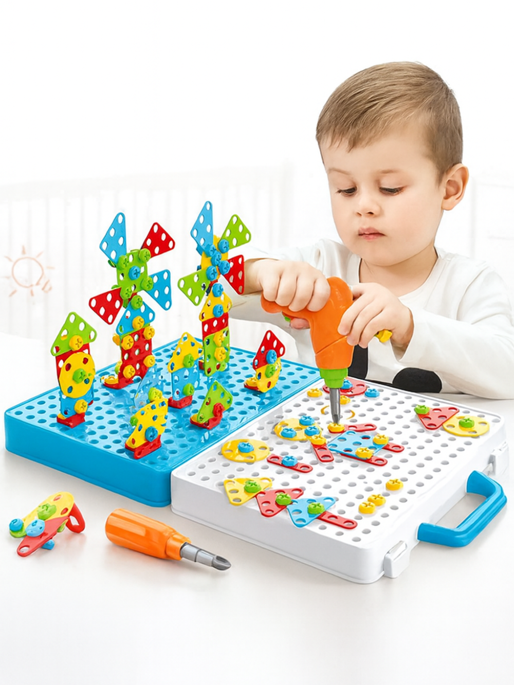 幼児が電動ドリルでネジを締めながら、水色のボード上にカラフルな羽根付き立体風車ブロックをいくつも並べている様子
