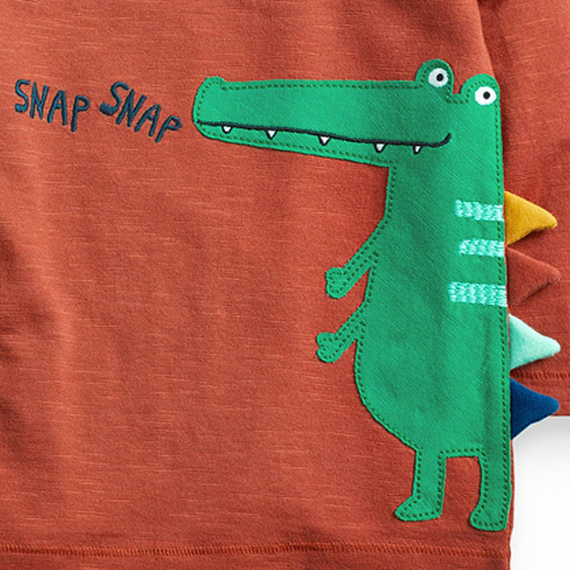 オレンジ長袖Tシャツ前面のワニプリントと「SNAP SNAP」ロゴを大きく写したクローズアップ
