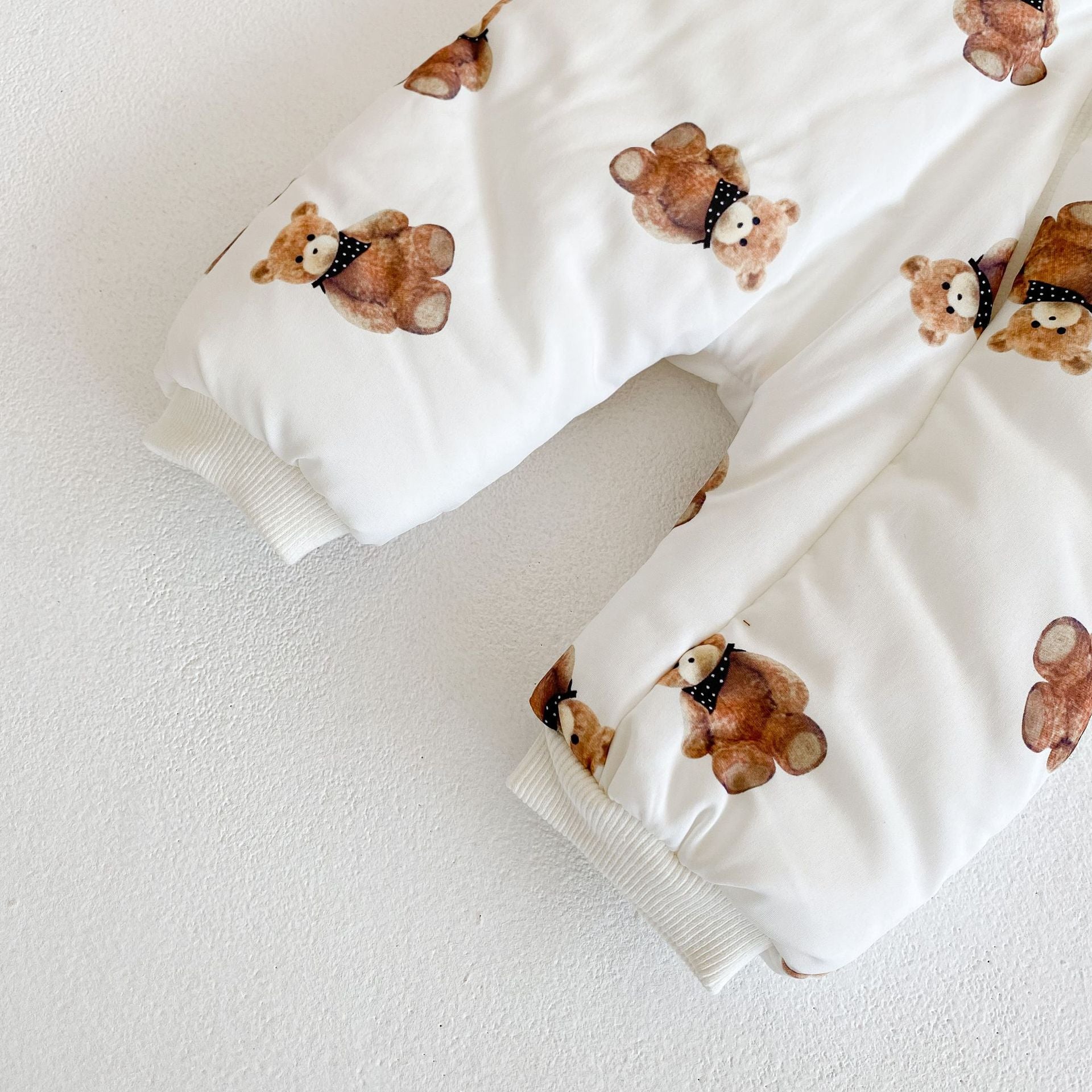 袖口と足元のリブカフスとくま柄プリントが見えるベビーカバーオール裾部分のクローズアップ
