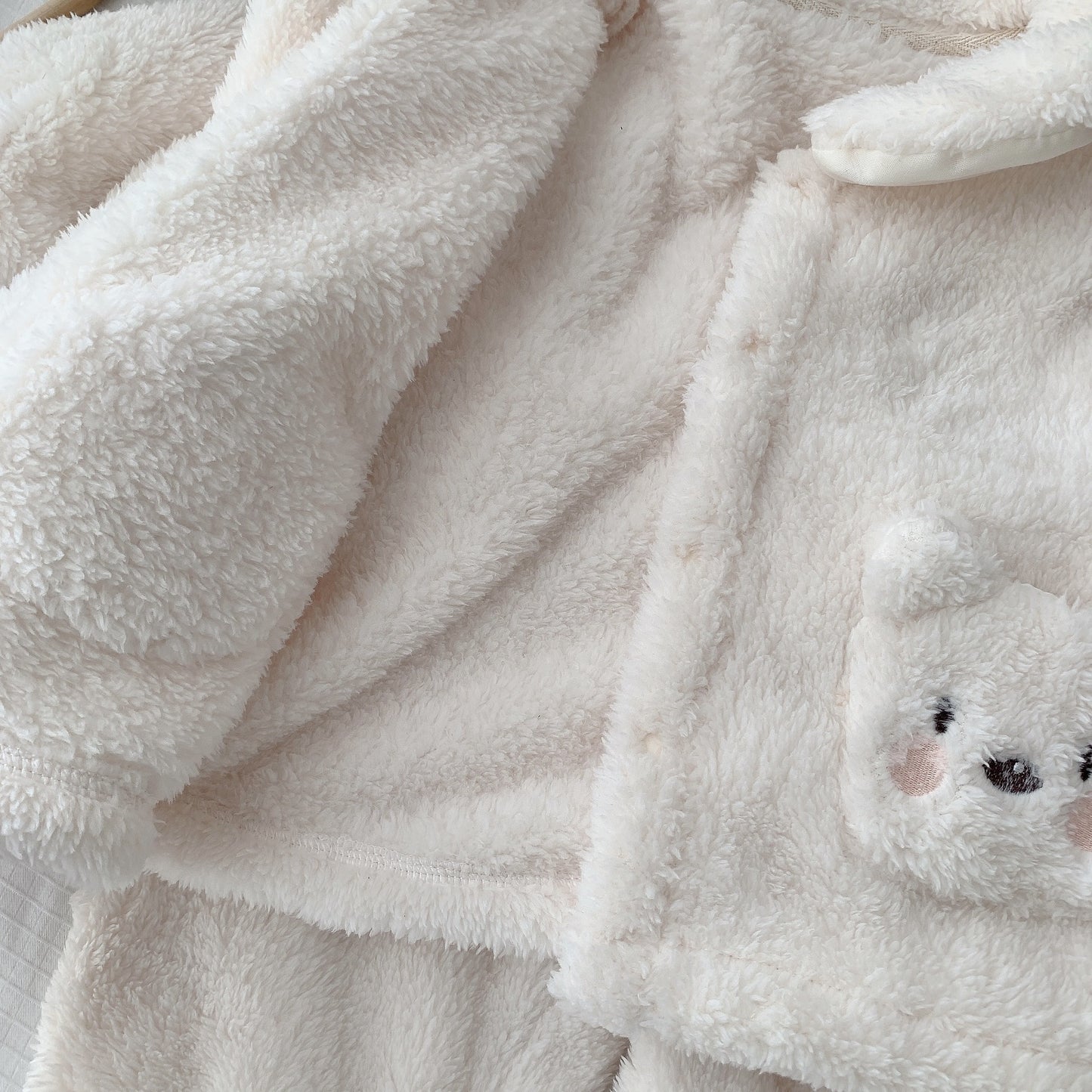 ホワイトボアジャケットの前立てと袖、くまフェイス刺繍ポケットが見える子ども用もこもこ上下セットのディテールクローズアップ
