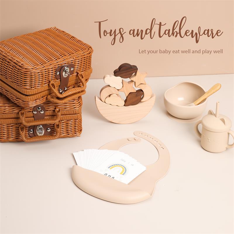 ラタン風バスケットが3段に積まれ、手前にベージュのシリコン食器セットとビブが並んでいる画像（ベビー用おもちゃ＆テーブルウェアセットのイメージ）
