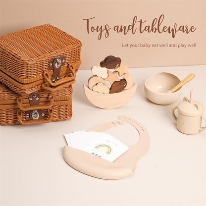 ラタン風バスケットが3段に積まれ、手前にベージュのシリコン食器セットとビブが並んでいる画像（ベビー用おもちゃ＆テーブルウェアセットのイメージ）
