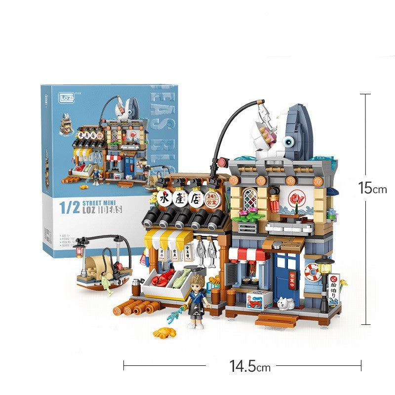 海鮮市場をテーマにしたミニブロックセット。巨大な魚の看板、木製フレームの2階建て店舗、青い引き戸、赤白ストライプの屋根、ホタテやタコの提灯、魚介類が並ぶ屋台カウンター、木箱や樽、小物フード、猫フィギュアと女性フィギュア付き。市場のにぎわいを細部まで再現した知育ビルディングトイ。サイズ14.5×15cm。
