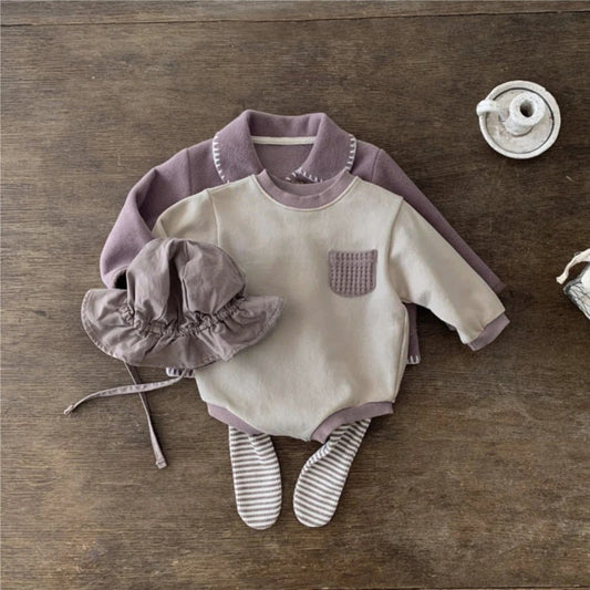 木目調の背景に置かれたライトアプリコットカラーの秋冬用ベビー長袖ロンパース正面
