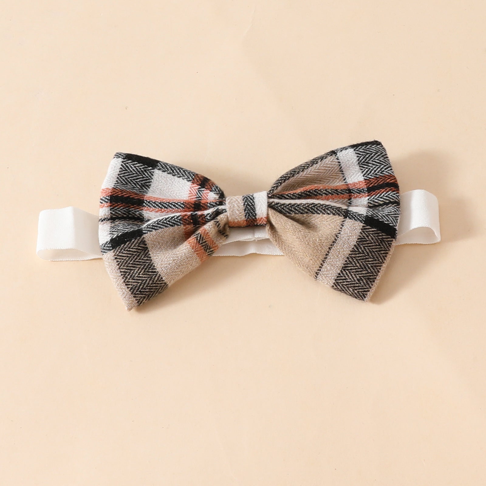 チェック柄リボンが付いたベージュ系ヘアバンドをアップで写したベビー用ヘッドアクセサリーの写真
