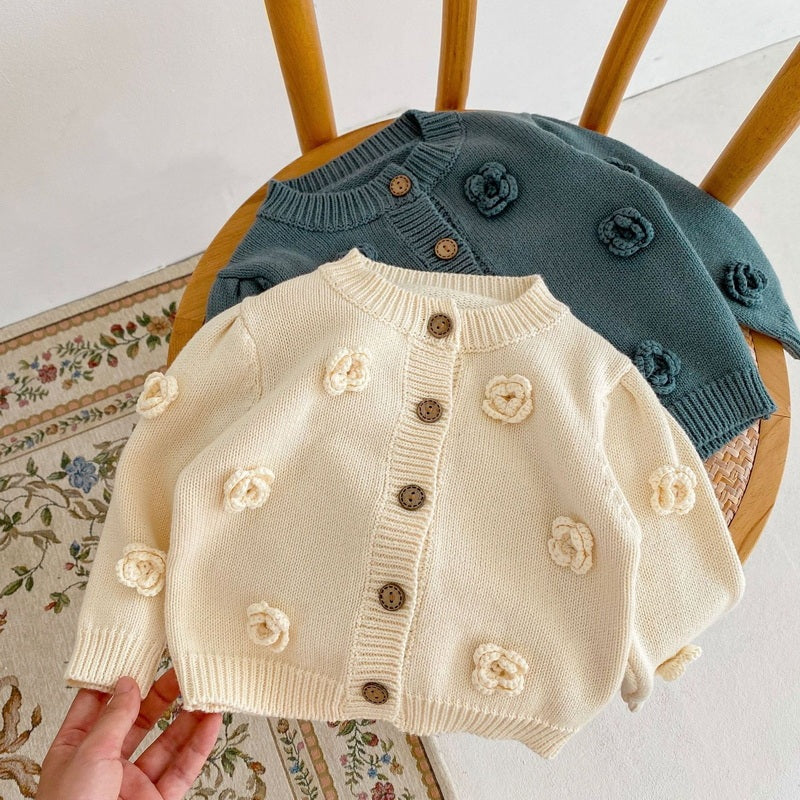 アプリコットカラーのフラワー編みベビーニットカーディガンを椅子の上に広げて撮影した画像  
