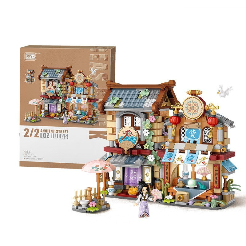 古代の商店街をテーマにしたミニブロックセット。木造フレームの二階建て建築、青瓦屋根、伝統的な商家の看板、色鮮やかな日除け布、店先の花飾り、提灯、樽や壺のディスプレイ、繊細な小物まで精密再現。時計台と白いハトのフィギュア、和装の人物フィギュア付き。細部の造形が美しい知育ビルディングトイ。幅約18cm。
