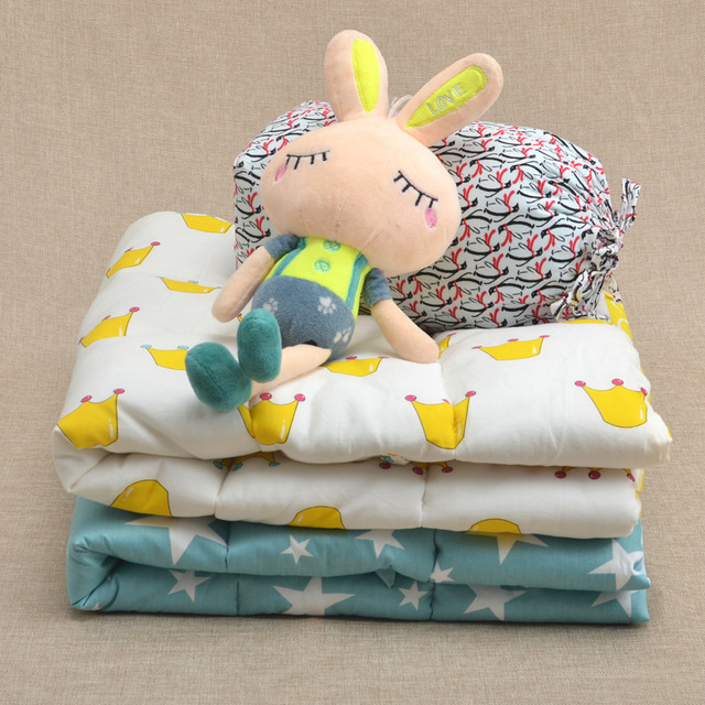 王冠柄デザインのベビーキルトブランケットを重ねて積み、その上にぬいぐるみを置いたやさしい雰囲気の写真（ベビーキルト 王冠柄 出産祝い）
