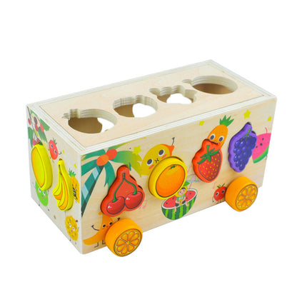 カラフルなフルーツ柄ブロックを荷台に積んだ木製トレーラーおもちゃが横向きに走るように配置された画像

