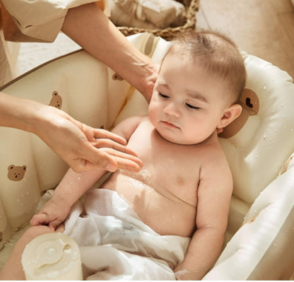 ベビーバスの縁に寄りかかった赤ちゃんがにこっと笑い、大人がそばで体を洗っているアップの写真（おうち沐浴中のベビーバスシーン）
