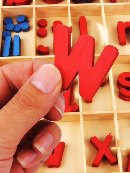 赤い小文字の木製文字ピースを指先でつまんで示す使用シーン
