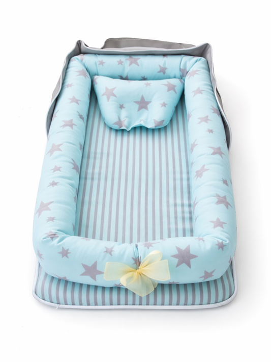 ブルー×グレーの星柄ベビーネスト（クッション枕付き）が、白背景のスタジオ撮影で縦向きに配置され、先端に淡いイエローのリボンが付いている商品画像。
