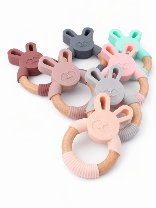 白背景に、ウサギ型シリコーンヘッドと木製リングを組み合わせたベビー用歯固め（6色セット）が重なるように並び、シリコーン部分の巻き付け（固定）デザインが見える商品画像。

