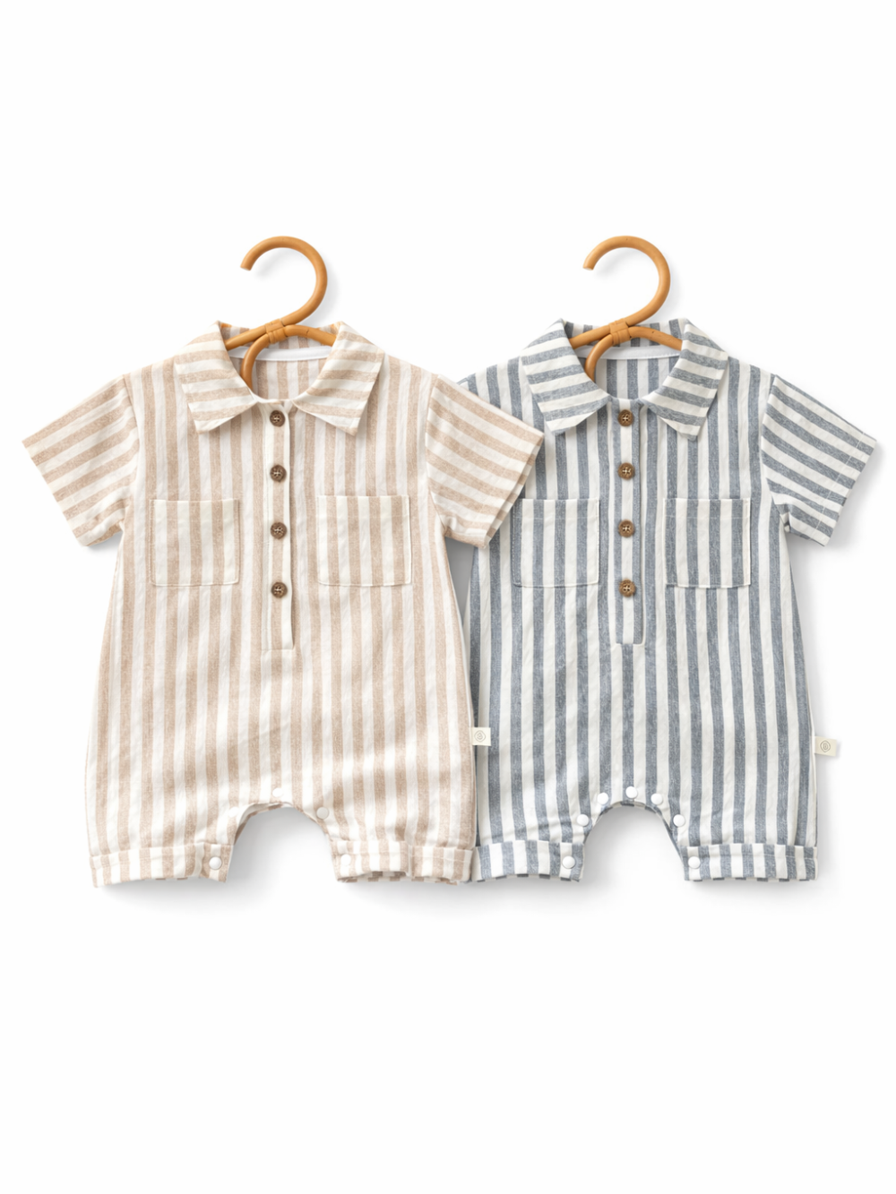白背景に、ストライプ柄の半袖襟付きベビーロンパース2点（ベージュ×ホワイト、グレー×ホワイト）が木製ハンガーに掛けて並べられ、前ボタンと胸ポケット、股下スナップのディテールが見える商品画像。
