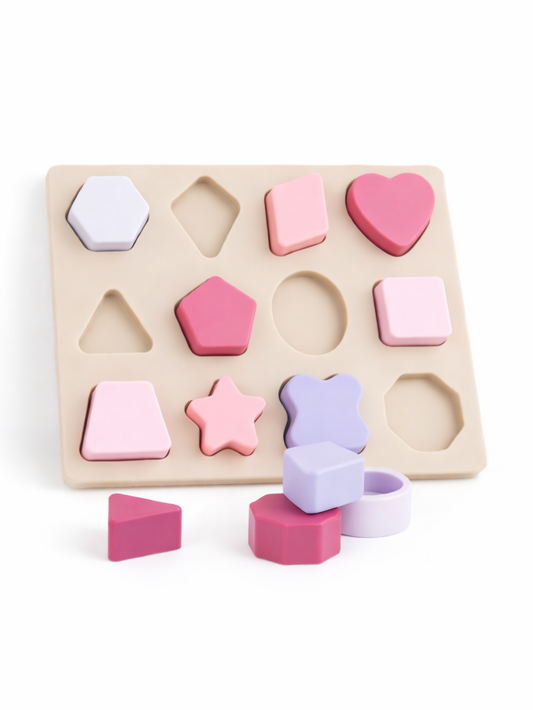 白背景のスタジオ撮影。ベージュの型はめパズルボードに、パステルカラー（ピンク／ラベンダー／白）の幾何学ブロックがはめ込まれ、手前にいくつかのブロックが置かれている。
