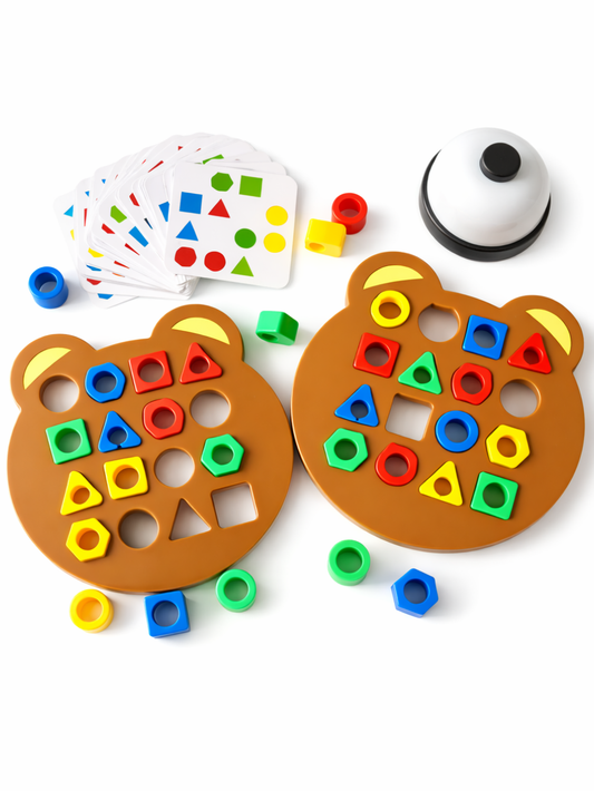 白背景のスタジオ撮影。クマ型の型はめボードが2枚並び、赤・青・黄・緑のカラフルな形パーツが差し込まれている。左上にお題カードの束、右上に白いベルがあり、周囲に追加のパーツが散らばっている。
