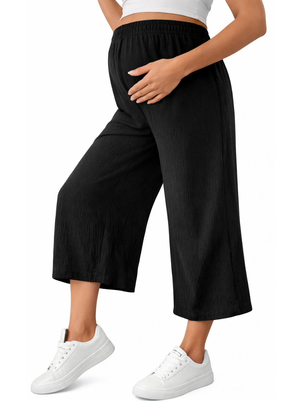 白背景のスタジオで撮影された、ウエストゴムのブラックのマタニティ用ワイドパンツ（クロップド丈）を白スニーカーと合わせた着用イメージ。
