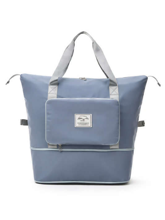 白背景のスタジオで撮影された、ライトブルーの大容量トートバッグ。グレーの持ち手と前面フラップポケット、ファスナー付きの下部収納、サイドベルトが付いている。
